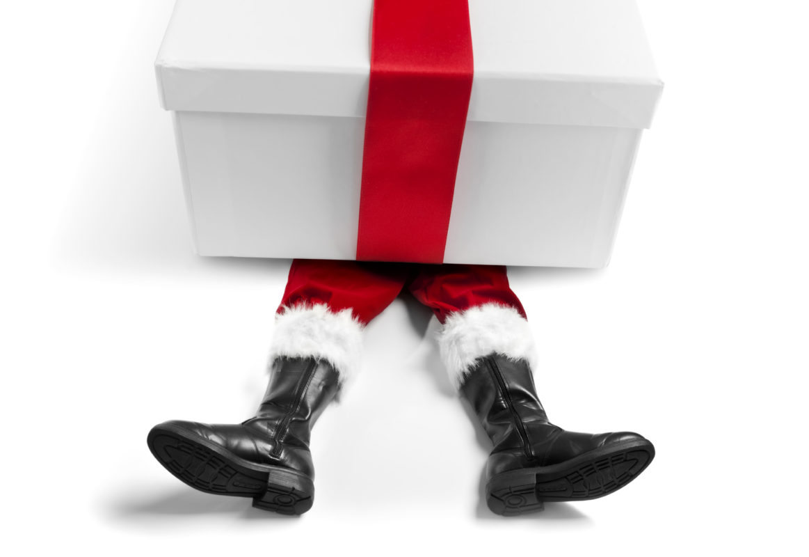 Concept image, showing Santa Claus red legs and white fur trim trousers, and black boots, trapped underneath a white Christmas present box, bound in a red ribbon.