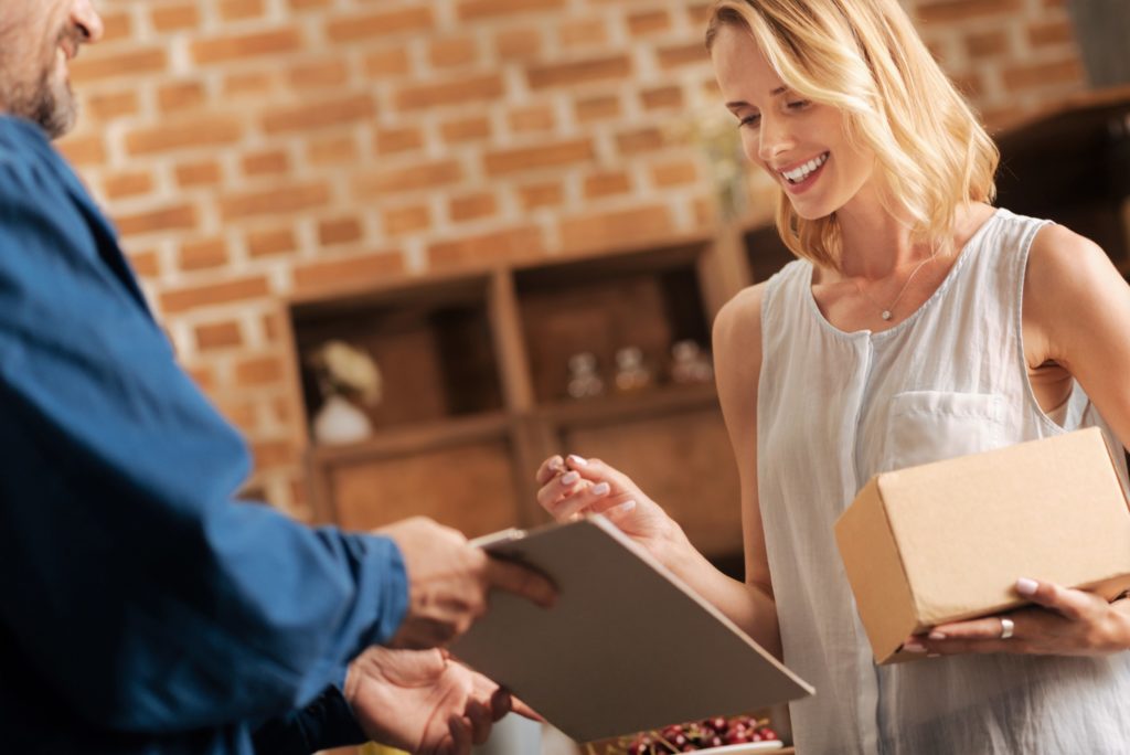 Blonde haired lady signing for collection of her online shopping, receiving a home delivery while signing some papers for the courier